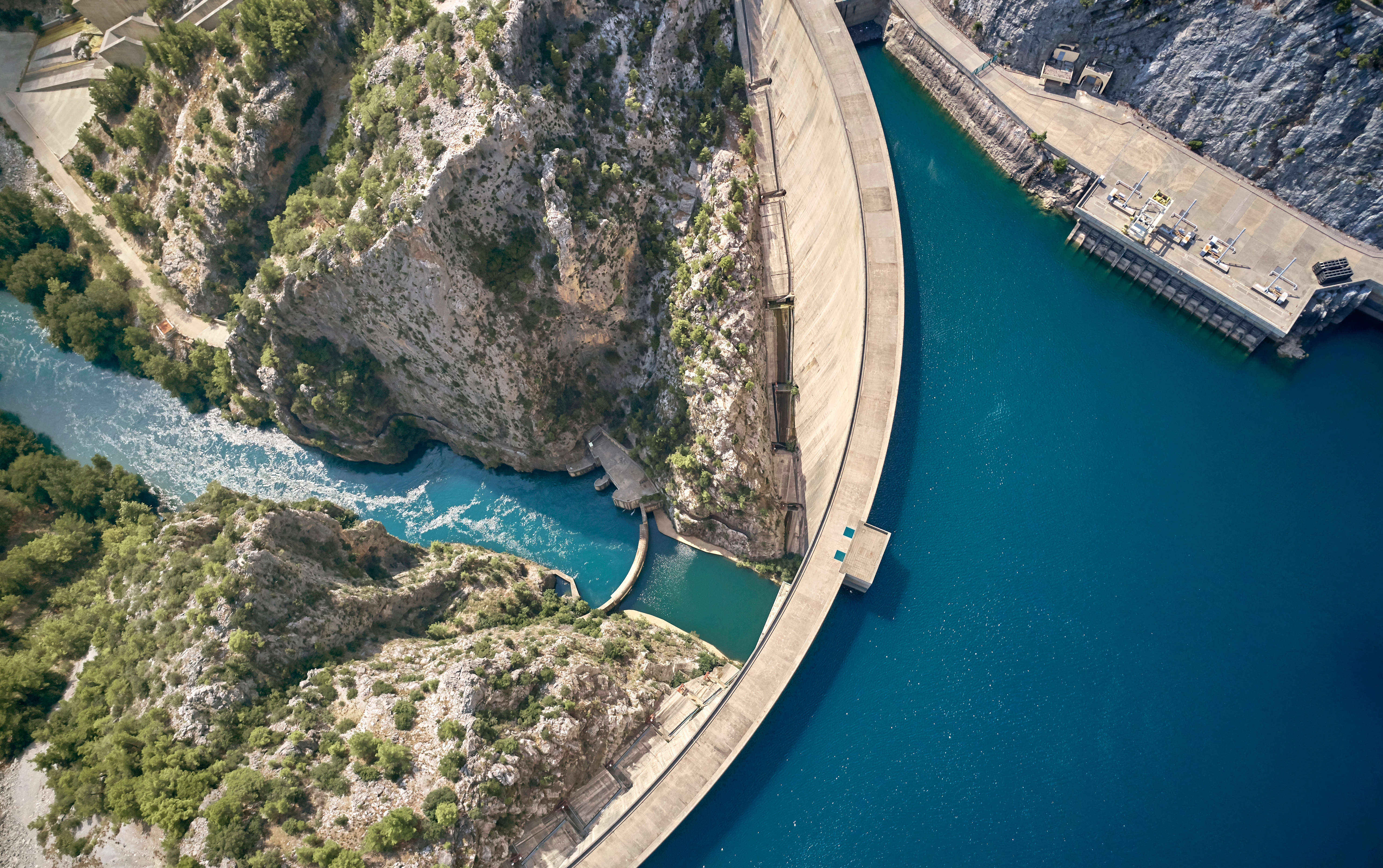 Aerial view of an arch concrete dam with the power intake and hydroelectric facilities located on the right side of the reservoir